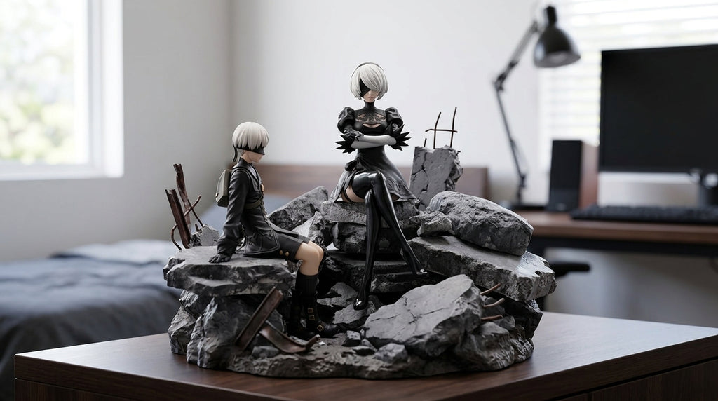 2B and 9S inspired figures displayed on rocky rubble diorama base on wooden desk with monitor and lamp visible in background gaming room setting