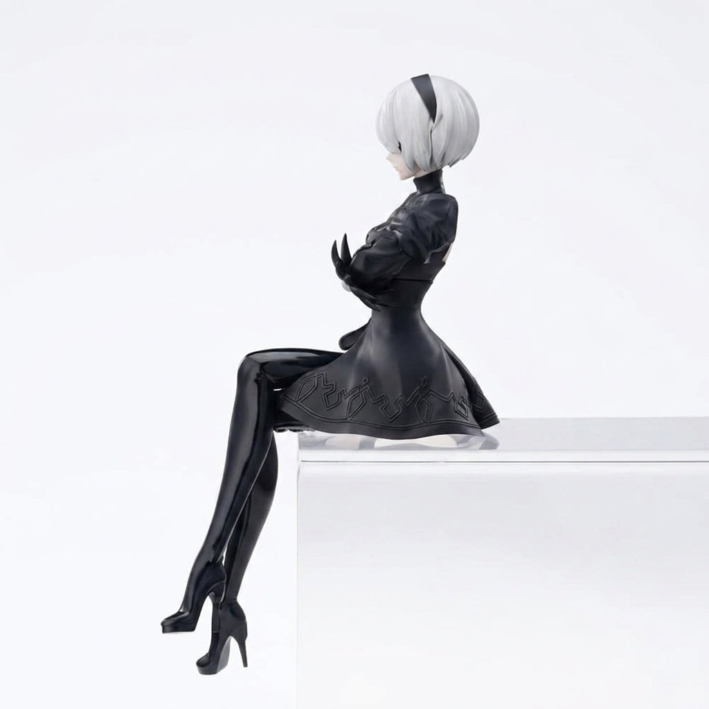 2B inspired PVC collectible figure side profile seated pose showing detailed black dress with embroidered hem white hair black headband and crossed arms on white background